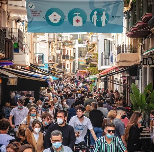 crowd in street wearing face masks underneath a banner with hygeine messages